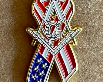 Puede incluir: Pin dorado en forma de cinta, con el diseño de la bandera estadounidense: rayas rojas y blancas, estrellas azules. Incorpora símbolos masónicos, incluyendo un compás, una escuadra y la letra "G".