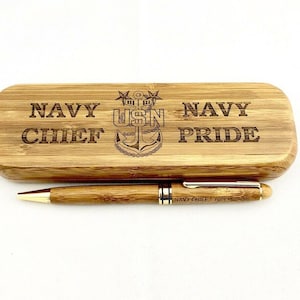 Op de afbeelding: Een houten pen en bijpassende etui. De pen heeft een goudkleurige punt en accenten. De etui is rechthoekig met afgeronde randen en is voorzien van de woorden "NAVY CHIEF NAVY PRIDE" en een USN-embleem.