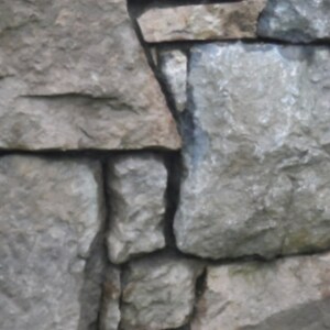 May include: A close-up of a stone wall made of various sized, irregularly shaped, gray and brown stones. The stones are stacked on top of each other to create a wall.