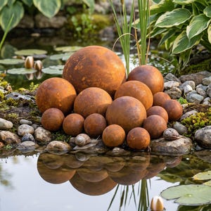 May include: A collection of spherical garden ornaments with a weathered, rusted metal finish. The spheres vary in size and are arranged in a cluster, displaying a textured, oxidized brown surface that contrasts with the surrounding natural environment.