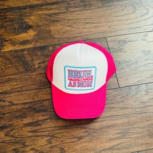 May include: A pink trucker hat with a white front panel and a pink mesh back. The hat features the text "BRUH. FORMERLY KNOWN AS MOM" in a blue and pink design.