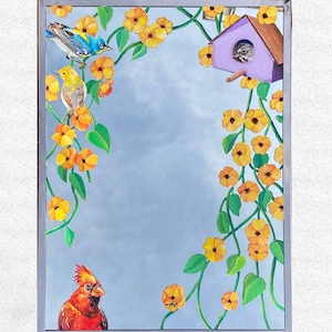 May include: A framed mirror with a painted scene of a cardinal, two small birds, a birdhouse, and yellow flowers. The mirror has a silver frame.