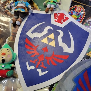 May include: A blue and red shield with a gold triangle and white wings. The shield is surrounded by plush toys, including a green and yellow character with a clock, a yellow character with a green dress, and a blonde character with a blue dress.