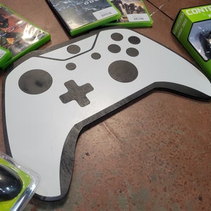 May include: A white and black wooden Xbox controller wall decor. The controller is a replica of the Xbox 360 controller.