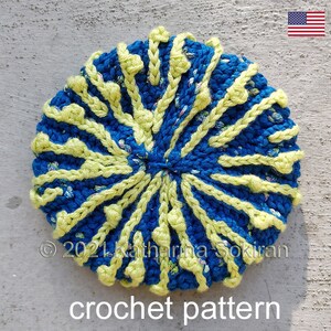 May include: A crochet pattern for a round, blue and yellow crocheted hat. The hat has a textured design with yellow stitches radiating out from the center. The text "crochet pattern" is written below the hat.