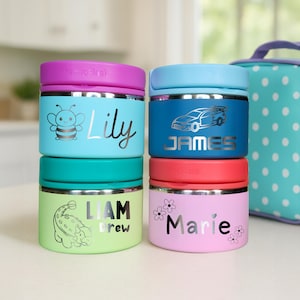 May include: Four colorful insulated food containers stacked together, each with a different name and design. The containers are light blue, green, pink, and dark blue, with silver accents. A matching lunch bag with white polka dots is in the background.