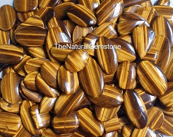 Könnte beinhalten: Ein großer Haufen polierter Tigerauge-Cabochons. Die Steine sind eine Mischung aus goldbraun und braun mit einem chatoyanten Effekt. Die Steine sind oval geformt und haben eine glatte, polierte Oberfläche.