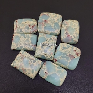 May include: A collection of eight light blue and white jasper cabochons with red and brown inclusions. The cabochons are rectangular and have a smooth, polished surface. Bulkgems is printed on the image.