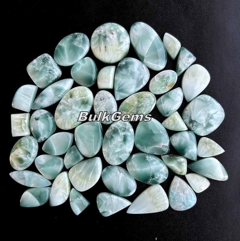 May include: A collection of 30 green and white cabochon gemstones. The stones are various shapes and sizes, with a smooth, polished finish. The stones are arranged in a circle on a black background. BulkGems is printed in white on the stones.
