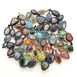 Pode incluir: Uma coleção de pingentes de pedras preciosas em várias formas e cores, cada um intrincadamente tecido com um cordão de macramê. Os pingentes apresentam pedras como olho de tigre, ametista e labradorita. O texto "Bulk Gems" é visível.