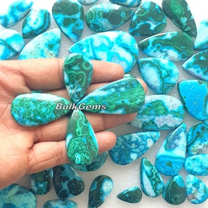 Puede incluir: Una colección de cabujones de piedras preciosas turquesa y verdes en forma de lágrima. Las piedras tienen un patrón de remolino de azul, verde y blanco.