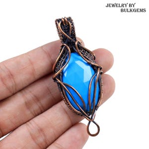 Puede incluir: Un colgante artesanal con una gema azul brillante facetada, encerrada en intrincado alambre de cobre. El alambrado forma una jaula decorativa alrededor de la piedra, con un lazo en la parte superior. Texto: JEWELRY BY BULKGEMS.