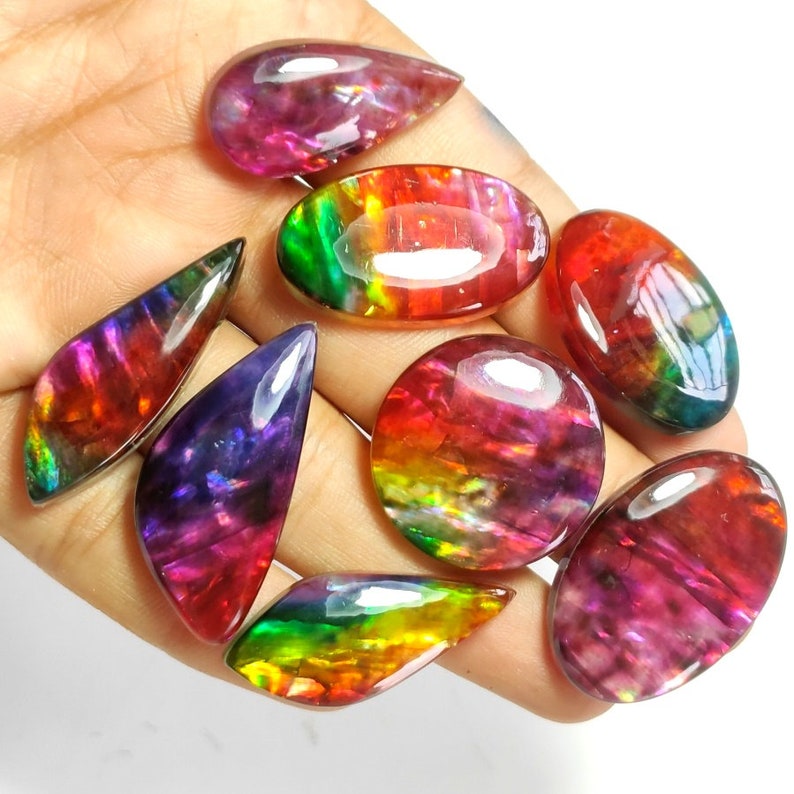 May include: A collection of eight iridescent gemstone cabochons in various shapes and sizes. The stones display a rainbow of colours, including red, orange, yellow, green, blue, and purple.