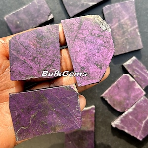 Op de afbeelding: Een verzameling van paarse en zwarte edelsteenplaten met een natuurlijke, ruwe afwerking. De platen zijn van verschillende groottes en vormen, met een unieke, iriserende glans. BulkGems is op een van de platen gedrukt.