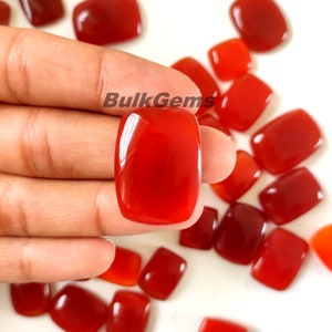 May include: A collection of red carnelian gemstones, cut into rectangular shapes, with a polished finish. The stones are displayed on a white surface.