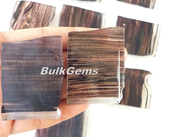 Puede incluir: Una colección de losas de ágata rayadas de color marrón y negro. Las losas tienen una forma irregular y un acabado pulido. Las losas están dispuestas en una mano, con el texto "BulkGems" visible en el centro.