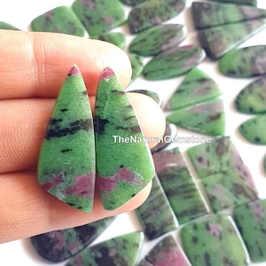 May include: Two green, pink and black gemstone cabochons in a teardrop shape. TheNaturalGemstone is printed on the image.