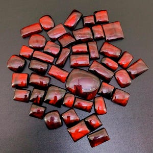 May include: A collection of red gemstone cabochons, with a variety of shapes and sizes. The stones have a deep red color and a glossy finish.