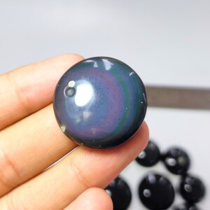 K&ouml;nnte beinhalten: Ein runder, irisierender Obsidian-Stein in dunkelblau, violett und gr&uuml;n. Der Stein hat einen wei&szlig;en Punkt in der Mitte.