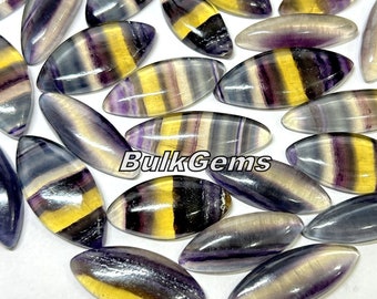 May include: A collection of oval-shaped, multi-colored fluorite gemstones. The stones have a variety of colors, including purple, yellow, and black. The stones are smooth and polished.