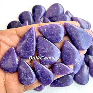 Puede incluir: Una colección de cabujones de piedra preciosa de lepidolita púrpura en forma de lágrima. Las piedras son lisas y pulidas, con un brillo sutil.