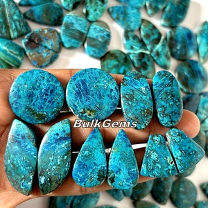 Puede incluir: Una colección de cabujones de turquesa en varias formas y tamaños, incluyendo redondos, ovalados y en forma de lágrima. Las piedras tienen un color azul verdoso con marcas marrones y blancas. Los cabujones se muestran en una mano.