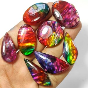 May include: A collection of iridescent gemstone cabochons in various shapes and sizes. The stones display a rainbow of colours, including red, orange, yellow, green, blue, and purple.