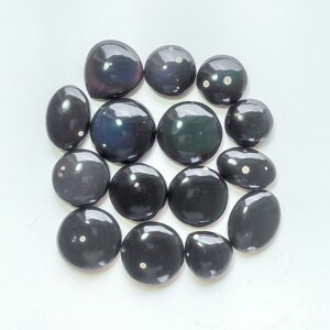 K&ouml;nnte beinhalten: Eine Sammlung von 15 schwarzen und wei&szlig;en Edelstein-Cabochons mit wei&szlig;en Flecken. Die Cabochons sind glatt und poliert und in einem Kreis auf wei&szlig;em Hintergrund angeordnet.