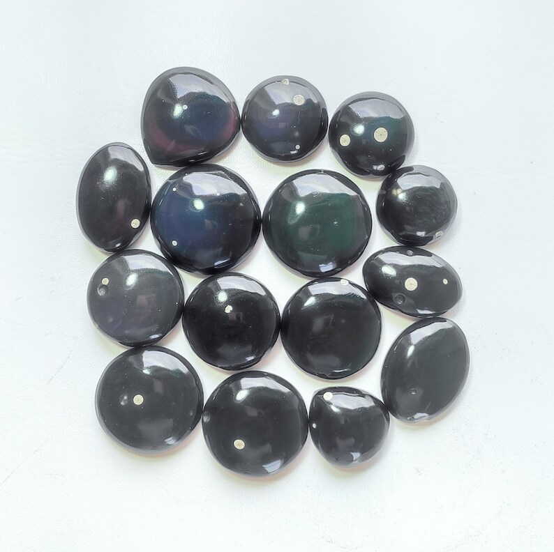 K&ouml;nnte beinhalten: Eine Sammlung von 15 schwarzen und wei&szlig;en Edelstein-Cabochons mit wei&szlig;en Flecken. Die Cabochons sind glatt und poliert und in einem Kreis auf wei&szlig;em Hintergrund angeordnet.