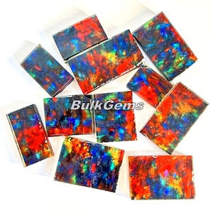 May include: A collection of ten rectangular pieces of opal, each with a different pattern of red, blue, green, and black. The opals are iridescent and have a metallic sheen.