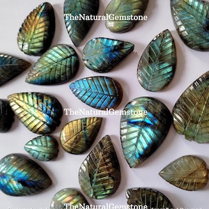 Può includere: Una collezione di 15 sculture di foglie in labradorite, una pietra preziosa iridescente verde e blu. Le sculture hanno tutte la forma di una lacrima con un motivo a foglia inciso sulla superficie. TheNaturalGemstone è stampato sull'immagine.