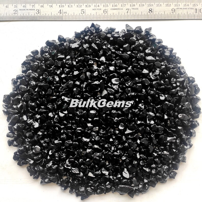 May include: A close-up view of a pile of black obsidian chips. The chips are various sizes and shapes, with a glossy finish. The chips are arranged in a circular pattern on a white surface.