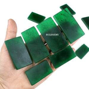 Puede incluir: Una colección de ocho piedras preciosas cabujón verdes, talladas en forma rectangular, dispuestas en una mano. Las piedras preciosas son lisas y pulidas, con una ligera variación de color.