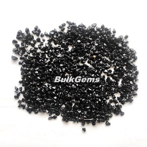May include: A close-up image of a pile of black obsidian chips. The chips are small and irregular in shape, and they have a shiny, glassy finish.