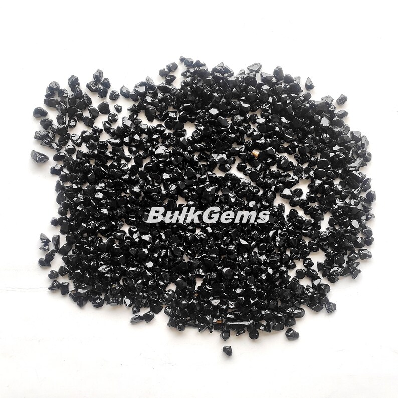 May include: A close-up image of a pile of black obsidian chips. The chips are small and irregular in shape, and they have a shiny, glassy finish.