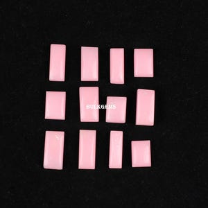 May include: A collection of 12 pink rectangular shaped gemstones. The gemstones are arranged in three rows of four. The gemstones are smooth and polished.