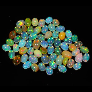 May include: A collection of oval-shaped opal gemstones in various shades of white, green, and yellow with iridescent rainbow flashes.