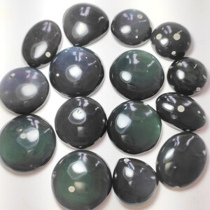 K&ouml;nnte beinhalten: Eine Sammlung von 15 glatten, runden, schwarzen und gr&uuml;nen Steinen mit wei&szlig;en Flecken. Die Steine sind in einem Kreis auf einer wei&szlig;en Oberfl&auml;che angeordnet.