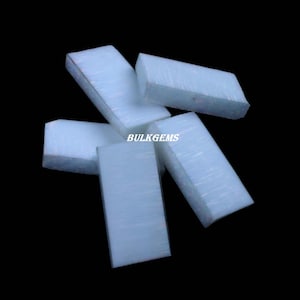 May include: A collection of rectangular, light blue gemstones with a translucent appearance. The gemstones are scattered against a black background. The text "BULKGEMS" is visible on one of the gemstones.
