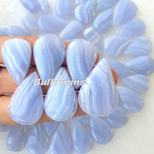 Puede incluir: Una colección de cabujones de ágata azul en forma de lágrima. Las piedras tienen un patrón de bandas blancas y azules. Los cabujones miden aproximadamente 2,5 cm de largo.