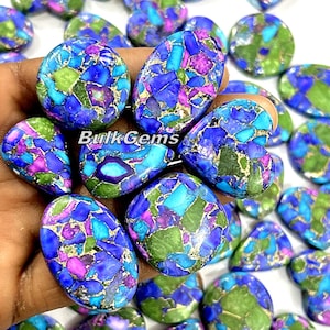 Pode incluir: Uma coleção de cabochões ovais de turquesa com uma mistura de cores azuis, verdes, roxas e douradas. As pedras têm um aspeto marmorizado e salpicado.