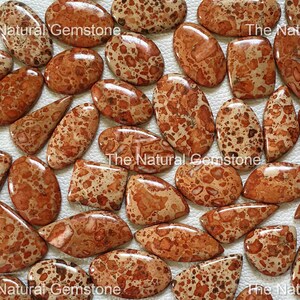 Puede incluir: Una colección de 20 cabujones de jaspe natural marrón y naranja con un patrón moteado. Los cabujones son de varias formas y tamaños, incluyendo ovalados, en forma de lágrima y rectangulares.