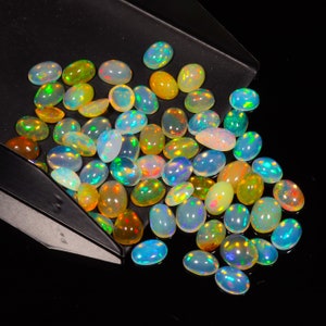 May include: A collection of oval-shaped opal gemstones in various shades of blue, green, yellow, and orange. The opals are iridescent and have a rainbow-like sheen.