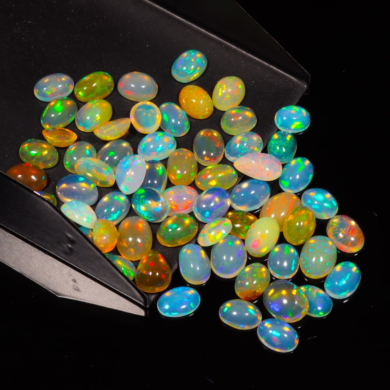 May include: A collection of oval-shaped opal gemstones in various shades of blue, green, yellow, and orange. The opals are iridescent and have a rainbow-like sheen.