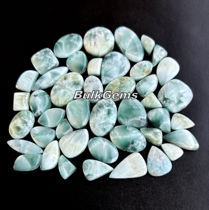 May include: A collection of 30 green and white cabochon gemstones. The stones are various shapes and sizes, including oval, teardrop, and square. The stones are polished and have a smooth, shiny finish.