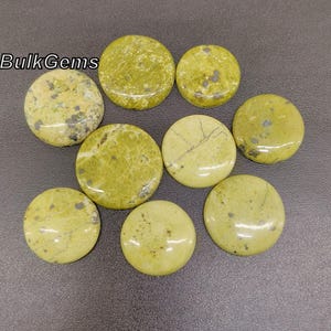 May include: A collection of nine round, polished gemstones in varying shades of green and yellow. The stones have unique patterns and textures, with some showing darker spots and veining. The text "Bulk Gems" is visible in the upper left corner.