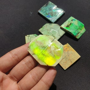 May include: A collection of six iridescent green and yellow opal cabochons, with a variety of shapes and sizes. The cabochons are set against a dark background.