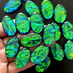 Może przedstawiać: Kolekcja owalnych, zielonych i niebieskich, opalizujących kaboszonów z opalu. Kamienie mają mieniący się, tęczowy efekt.