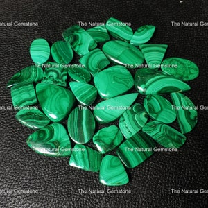 Può includere: Una collezione di 17 cabochon di malachite verde, ognuno con motivi a spirale unici. Le pietre sono di varie forme e dimensioni, alcune sono ovali, a forma di lacrima e rettangolari.