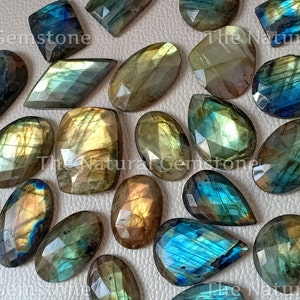 Può includere: Una collezione di cabochon di labradorite in varie forme e dimensioni. Le pietre hanno un colore blu-verde iridescente con bagliori dorati.